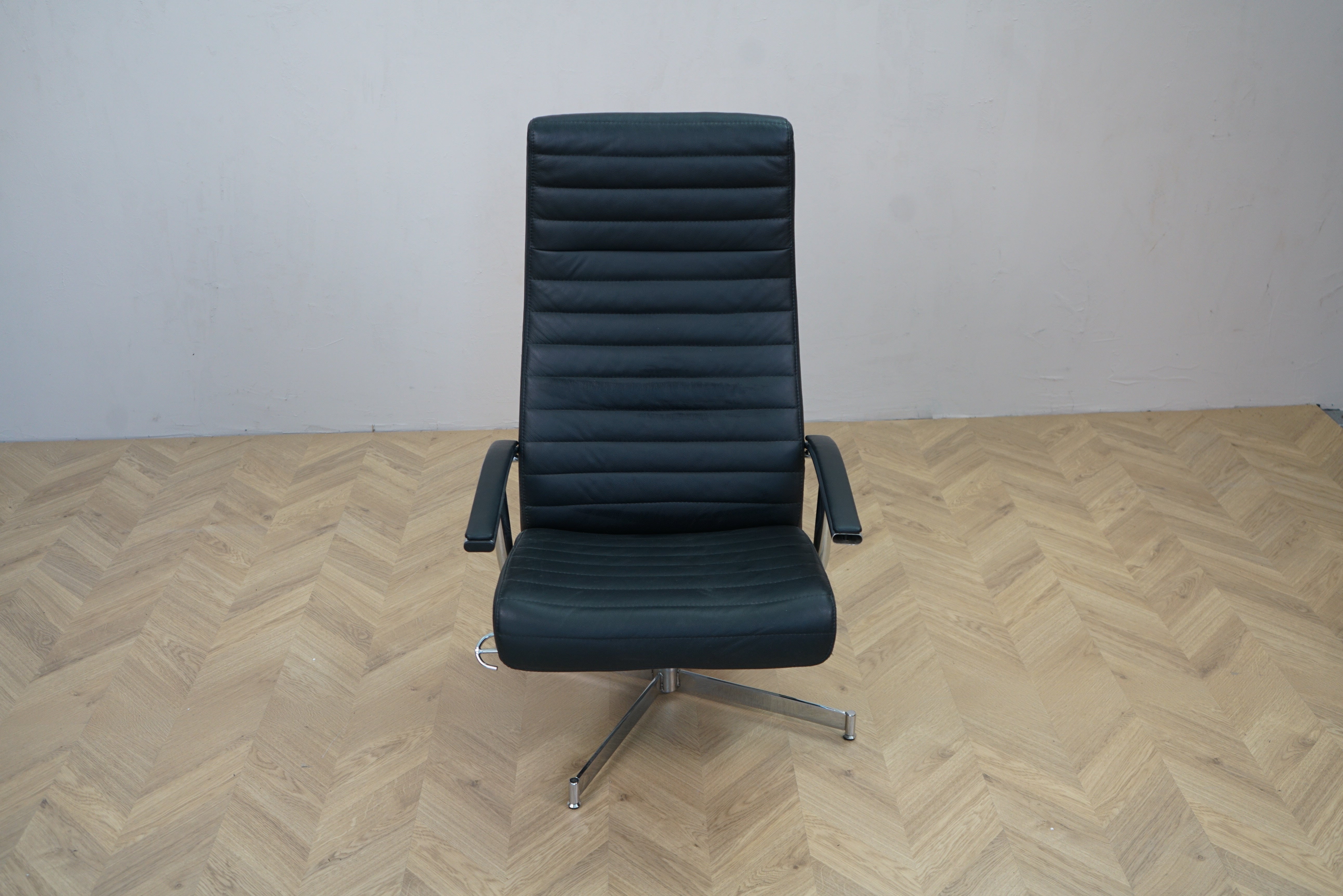 Sort læder loungestol med høj ryg, armlæn og drejefod set forfra